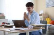 © New Africa - Happy student with clasped hands praying for good exam result at table indoors