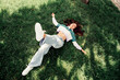 © deagreez - Young woman lying on grass outdoors in trendy casual outfit during spring, expressing joy and relaxation in natural light