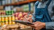 © Ilona - A worker wearing a blue apron is taking notes on a clipboard while surrounded by boxes of food items in a busy grocery warehouse during the afternoon