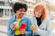 © Jose Calsina - Two cheerful girls are engaging with their mobile phones, making a purchase using a credit card, and enjoying a delightful shopping experience together while sharing smiles and excitement.