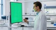 © cila - Male research scientist in a lab coat working on a computer with a green screen display in a modern science laboratory.