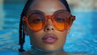 © ika ndari - Close-up of a woman's face in a pool, wearing large orange sunglasses