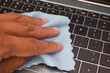 © Maule - Hand cleaning laptop keyboard with blue microfiber cloth, concept of hygiene, device care, and electronic maintenance.