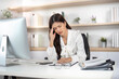 © wichayada - Workplace Stress. Young woman experiencing headache while working at her desk.