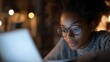 © Tujuenam - Focused young woman working late on her laptop illuminated by the screen's light