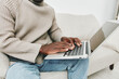 © SHOTPRIME STUDIO - A young Black man working on a laptop while seated on a cozy couch, wearing a beige sweater and casual jeans, depicting a relaxed and productive home environment