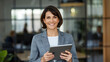 © Arpon - Confident businesswoman in a gray suit smiling while using a tablet in a modern office, representing leadership, technology, and corporate success
