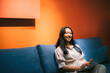 © Westend61 - Smiling woman using laptop on sofa indoors with orange wall