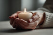© Irakli - in dimly lit room hands gently cradle lit candle radiating warmth and calm