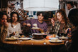 © qunica.com - A group of close friends sharing a warm meal together around a cozy dinner table, enjoying each other's company and a lively atmosphere.