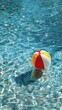 © horizon - Colorful red, yellow, and white beach ball creates gentle ripples as it floats in the inviting, shimmering blue water of a resort swimming pool on a sunny day.