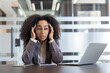 © Tetiana - Tired and overwhelmed young African American woman sitting at her desk in the office and holding her head in her hands