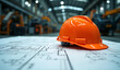 © Rhony - Orange industrial safety helmet is placed on a blueprint inside the factory.