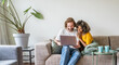 © Davide Angelini - Multiracial young couple watching computer laptop sitting on the sofa at home - Happy diverse husband and wife using pc online services - Technology life style concept