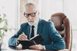 © deagreez - Confident senior businessman planning his work schedule in a luxurious office environment