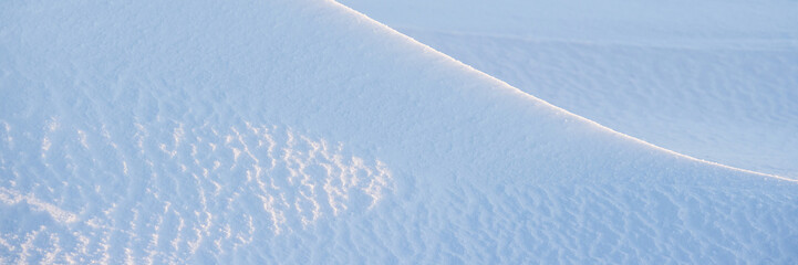 Wall Mural - Beautiful winter background with snowy ground. Natural snow texture. Wind sculpted patterns on snow surface. Wide panoramic texture for background and design. Closeup top view with copy space.