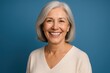 © Jelena - Radiant senior woman with silver hair displaying perfect smile and confident expression isolated on soft blue studio background