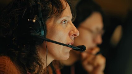 Medium shot of interpreters focused face as they read script via monitor headset mic visible background booth equipment gently blurred.