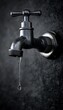 © B one - Close-up of a dripping outdoor faucet.  A single water drop hangs from a worn, metallic faucet.  Dark background