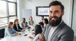 © Dev Forge - Bearded man in suit smiling in foreground with diverse team at conference table in background