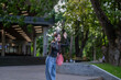 © Apichat - Young woman talking on phone and waving in park near university building