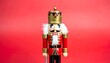 © DelightGrid - Traditional wooden nutcracker in red, gold, and blue uniform stands against solid red backdrop—evoking festive charm, craftsmanship, and cultural symbolism of the holiday season.