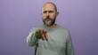 © Krakenimages.com - Bearded bald man in a gray sweater gestures pointing forward against a purple background, displaying a serious expression.