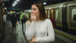 © Krakenimages.com - Young woman with blonde hair looking anxious at an indoor train station with blurred passengers and train in the background, capturing urban transit atmosphere.