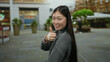 © Krakenimages.com - Woman smiling and giving thumbs up on city street with urban backdrop and modern buildings highlighting a lively urban environment with greenery.