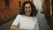 © Krakenimages.com - Middle age hispanic woman smiling in white shirt gives thumbs up in an old town street showing happiness outdoors with rustic urban background and historic architecture.