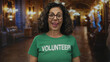 © Krakenimages.com - Middle age hispanic woman volunteer wearing green t shirt with volunteer text sticks tongue out in museum hall; playfulness humor engagement.