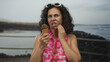 © Krakenimages.com - Woman in bikini with hawaiian lei by the seaside promenade holds ice cream with discomfort expression in beach setting.