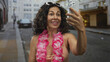© Krakenimages.com - Middle age hispanic woman in pink bikini blows kiss to camera while holding smartphone on a busy city street; affection flirtation joy.