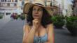 © Krakenimages.com - Hispanic middle-aged woman in a bikini and straw hat stands thoughtfully on an outdoor street.
