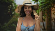 © Krakenimages.com - Hispanic woman in a bikini enjoys an ice cream outdoors in a green park, wearing a sun hat and smiling happily in a vibrant summer setting.