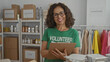 © Krakenimages.com - Woman in volunteer uniform writing on clipboard in charity room with clothes and food donations shelves.