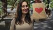 © Krakenimages.com - Woman in park holding paper bag with heart design surrounded by green trees outdoors smiling happily.