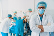 © Dorde - Confident Male Doctor in Surgical Attire Standing in a Busy Hospital Operating Room
