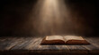 © Chaiwit - Old rustic book lies open on weathered wooden table with warm beam of light shining down, creating peaceful and nostalgic mood