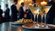 © Pete - Elegant martini cocktails with olives, lemon twists served at corporate event. Business people in suits network in blurred background. Sophisticated celebration, luxury hospitality, social gathering