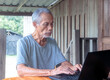 ©  Mushroom House - Senior man using laptop on rustic porch, embracing digital life in a peaceful rural setting.