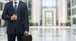 © Dezayn - Confident Businessman in a Suit Holding a Briefcase in a Modern Office Lobby