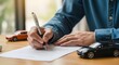 © MSTHIRAMONY - A persons hands signing a document with a pen, with miniature black and orange sports cars placed on a wooden desk, suggesting car insurance or purchase