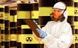 © Grispb - Nuclear energy, Hazardous waste, Industrial safety. Worker in protective suit and respirator with clipboard inspecting barrels of radioactive waste in storage facility.