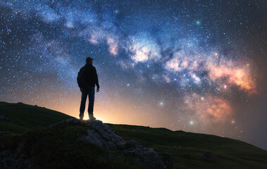 Wall Mural - Glowing Milky Way and man on mountain peak at starry night. Silhouette of a guy on the hill, sky with bright stars. Galaxy. Space landscape with milky way. Nightscape. Travel background. Concept