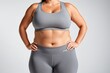 © Michael - Frau mit sportlicher Kleidung und Plus-Size-Figur zeigt selbstbewusst ihre Körpermitte vor neutralem Hintergrund