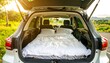 © Jesika - Cozy camping setup with a bed in an SUV parked on a scenic road surrounded by greenery