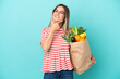 © luismolinero - Young woman holding a grocery shopping bag isolated on blue background happy and smiling