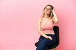 © luismolinero - Young woman sitting on a chair over isolated pink background having doubts and with confuse face expression