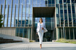 © Stock 4 You - Full body portrait of indian or Latin good looking middle aged leader female businesswoman. Young hispanic woman in stylish business clothes walking outdoor at modern office building. Copy space